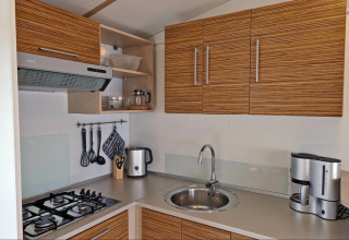 Cocina moderna en alojamiento glamping, con estufa, fregadero, hervidor y cafetera en la encimera.