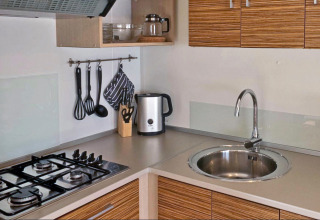 Cocina moderna en glamping con estufa de gas, fregadero, hervidor, utensilios y armarios de madera.