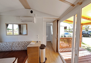 Interior de una cabaña con sofá, aire acondicionado, espejo, baño abierto y acceso a la terraza.