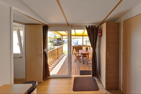 Entrada de una acogedora cabaña con terraza de madera y comedor exterior bajo techo amarillo.