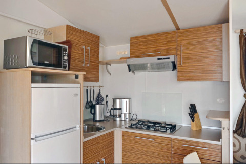 Cucina moderna da glamping con mobili in legno, piano cottura a gas, frigo e microonde.
