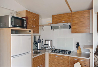 Cucina moderna da glamping con mobili in legno, piano cottura a gas, frigo e microonde.