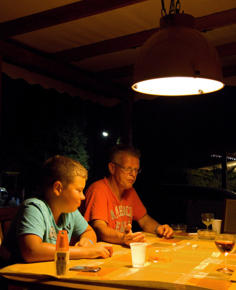 Dos personas sentadas en una mesa bajo una lámpara en un lodge por la noche, jugando a los dados.