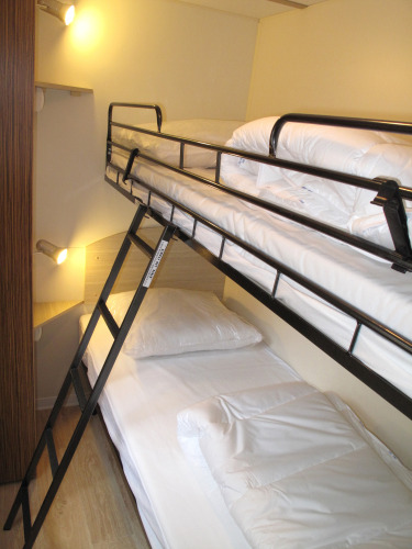 Een foto van een modern stapelbed met witte dekbedden in een glampingaccommodatie met wandlampen.