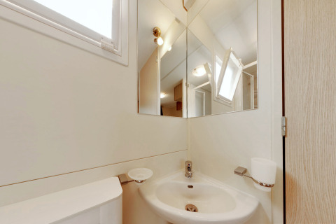 Baño moderno con espejo, lavabo, ventana abierta y vaso para cepillos en SunLodge Maple, Italia.