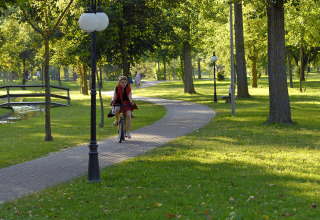 A woman rides a bicycle on a tree-lined path in a park at Camping Pra'delle Torri in Veneto, Italy.