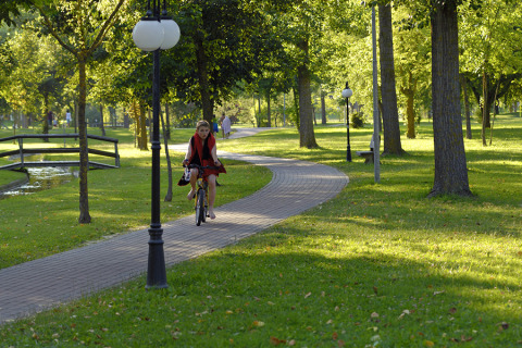 A woman rides a bicycle on a tree-lined path in a park at Camping Pra'delle Torri in Veneto, Italy.