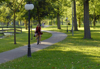 A woman rides a bicycle on a tree-lined path in a park at Camping Pra'delle Torri in Veneto, Italy.