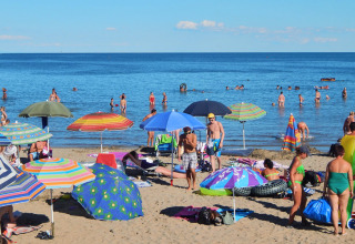 Fyldt strand med farverige parasoller og badende gæster på Camping Pra'delle Torri, Veneto, Italien.