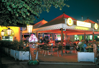 Outdoor dining area at Camping Pra'delle Torri holiday park in Veneto, Italy, illuminated at night with guests.