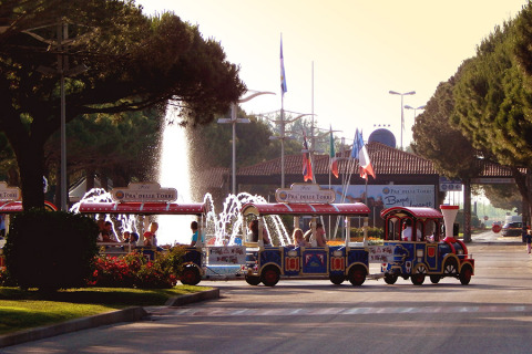 A colorful mini train with families passes by a fountain at Camping Pra’delle Torri holiday park in Veneto, Italy.