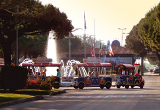 A colorful mini train with families passes by a fountain at Camping Pra’delle Torri holiday park in Veneto, Italy.