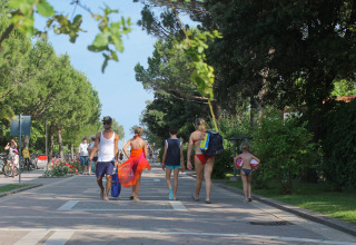 Families in swimwear stroll along a leafy path at Camping Pra'delle Torri holiday park in Veneto, Italy.