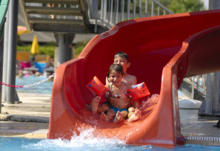 Due bambini si divertono su uno scivolo rosso in piscina al Camping Pra'delle Torri, Veneto, Italia.