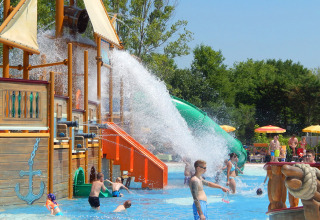 Children and adults play at a water park with a pirate ship, water slide, and splash features at Camping Pra’delle Torri.