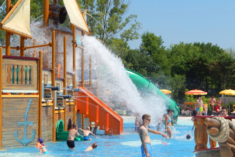 Enfants et adultes s’amusent dans un parc aquatique avec bateau pirate et toboggan au Camping Pra’delle Torri, Italie.
