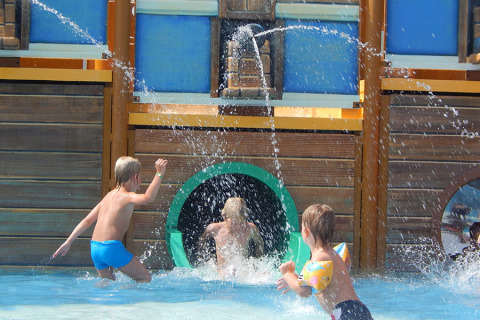 Kinderen spelen en zwemmen onder waterstralen bij een piratenschip speeltuin op Camping Pra'delle Torri, Veneto.