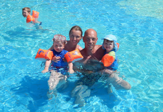 Famiglia che si diverte in piscina al Camping Pra'delle Torri, Veneto, Italia, con braccioli e costumi colorati.