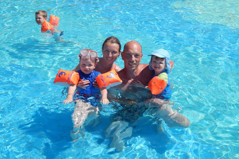 Familia disfrutando de la piscina en Camping Pra'delle Torri en Véneto, Italia, usando flotadores y gorros.