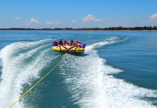 People enjoy a banana boat ride on clear water, being towed by a speedboat at Camping Pra'delle Torri.