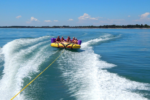 Personas se divierten en una banana inflable remolcada por un bote en Camping Pra'delle Torri, Italia.