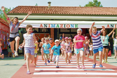 Bambini e adulti corrono felici all'aperto al Camping Pra'delle Torri, parco vacanze in Veneto, Italia.