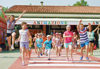 Bambini e adulti corrono felici all'aperto al Camping Pra'delle Torri, parco vacanze in Veneto, Italia.