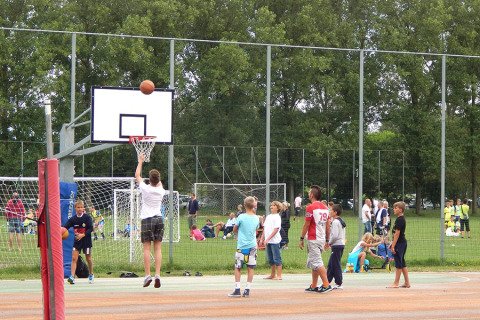 Niños juegan al baloncesto en una cancha al aire libre en Camping Pra'delle Torri, Véneto, con gente de fondo.