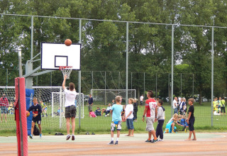 Children play basketball on an outdoor court at Camping Pra'delle Torri, Veneto, with people in the background.