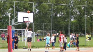 Niños juegan al baloncesto en una cancha al aire libre en Camping Pra'delle Torri, Véneto, con gente de fondo.