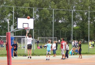 Niños juegan al baloncesto en una cancha al aire libre en Camping Pra'delle Torri, Véneto, con gente de fondo.