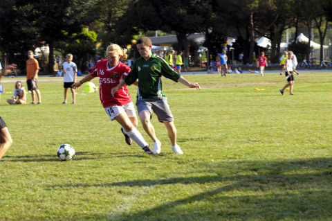 Soccer players in action on a grassy field at Camping Pra'delle Torri in Veneto, Italy, during a sunny day.