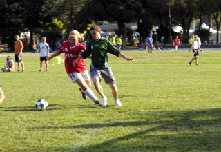 Soccer players in action on a grassy field at Camping Pra'delle Torri in Veneto, Italy, during a sunny day.