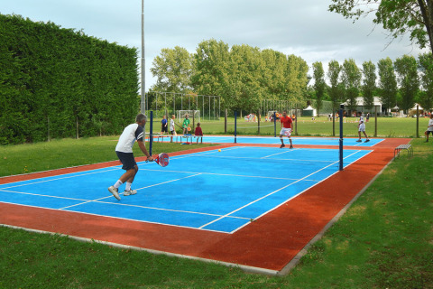 People play padel tennis on a blue court at Camping Pra'delle Torri holiday park in Veneto, Italy.