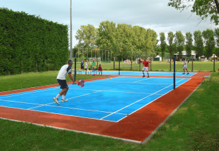People play padel tennis on a blue court at Camping Pra'delle Torri holiday park in Veneto, Italy.