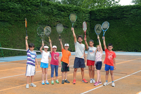 Children and a coach raise tennis rackets on a court at Camping Pra'delle Torri holiday park in Veneto, Italy.