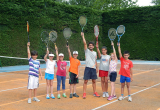 Børn og en instruktør holder ketsjere oppe på en tennisbane i Camping Pra'delle Torri i Veneto, Italien.