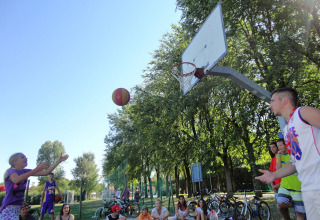 Børn og voksne spiller basketball på en udendørs bane under solskin i Camping Pra'delle Torri, Veneto, Italien.