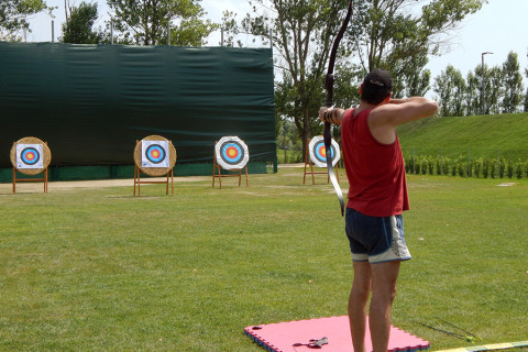 Arcere in maglia rossa tira con l’arco verso i bersagli al Camping Pra'delle Torri, Veneto, Italia.