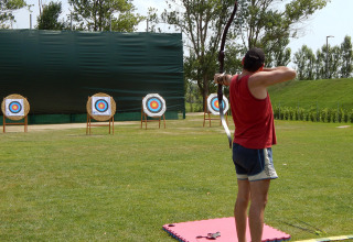An archer in a red shirt aims at multiple targets during archery at Camping Pra'delle Torri in Veneto, Italy.