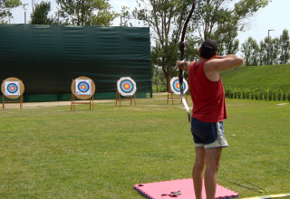 Persona en camiseta roja practica tiro con arco hacia dianas en Camping Pra'delle Torri, Veneto, Italia.