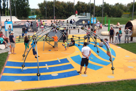 Niños y adultos jugando en un colorido parque infantil en Camping Pra'delle Torri, Véneto, Italia.