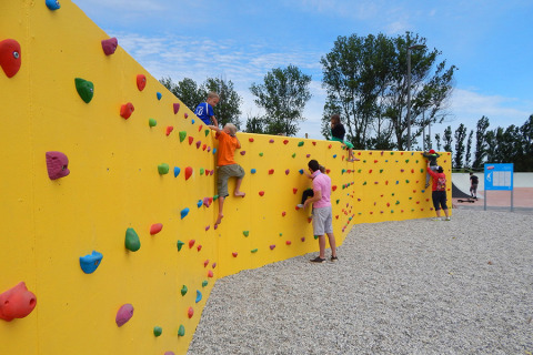 Niños y adultos trepando en un colorido muro de escalada en Camping Pra'delle Torri en Véneto, Italia.