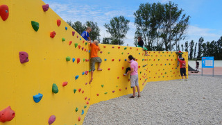 Niños y adultos trepando en un colorido muro de escalada en Camping Pra'delle Torri en Véneto, Italia.