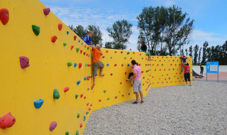 Children and adults climbing colorful climbing wall at Camping Pra'delle Torri holiday park in Veneto, Italy.