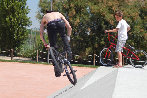 Two people riding BMX bikes in a skatepark at Camping Pra'delle Torri in Veneto, Italy, on a sunny day.