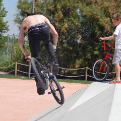 Dos personas montan bicicletas BMX en un skatepark de Camping Pra'delle Torri, Véneto, Italia, en un día soleado.