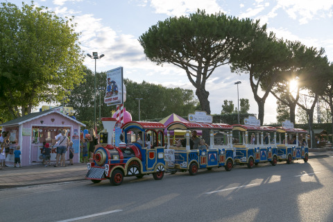 Tren infantil en Camping Pra'delle Torri, Véneto, Italia, con familias disfrutando una tarde soleada.