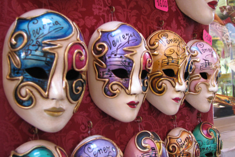 Máscaras venecianas decorativas a la venta, fotografiadas cerca de Caorle, Véneto, Italia, con diseños coloridos.