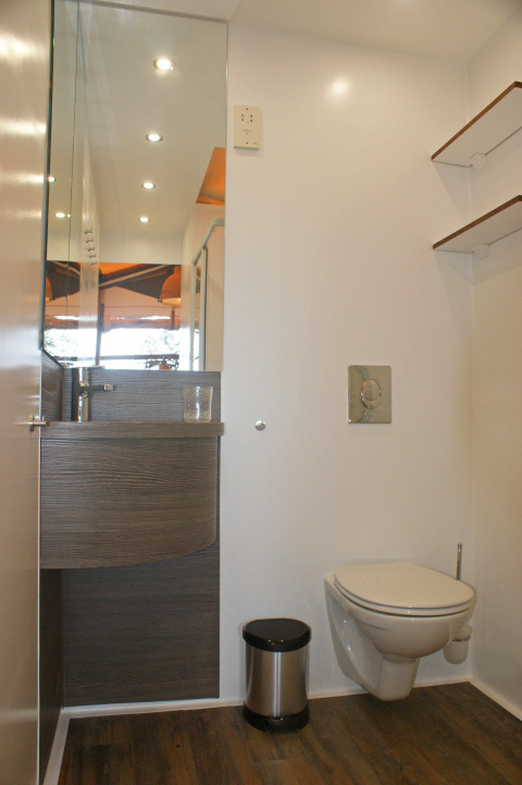 Baño moderno en SunLodge Safari, Camping Pra’delle Torri, Italia, con inodoro suspendido y espejo grande.